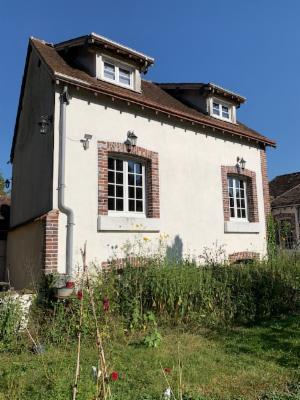 Maison de brique et d'enduit clair à deux lucarnes, jardin en friche au premier plan