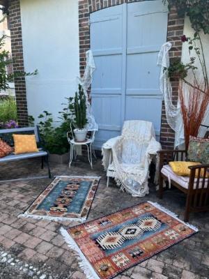 Terrasse pavée devant des volets bleus, tapis anciens, fauteuils et coussins