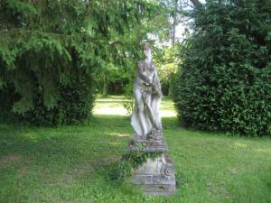 Statue de pierre sur son socle, au milieu de la pelouse du parc, devant des conifères
